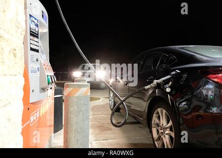 Fueling up at a gas station at night; oncoming vehicle with headlights on; gassing up; filling up the car.