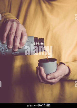 A mid section of a girl wearing yellow clothing pouring a hot cup of coffee or tea from a thermos flask Stock Photo