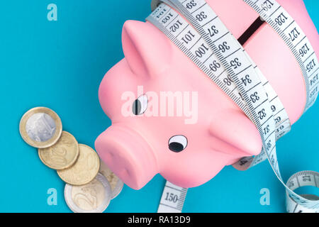 Investments and metering or counting idea. Ceramic toy pig with white flexible ruler on blue background. Financial diet concept. Stock Photo