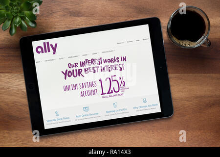 The website of Ally bank is seen on an iPad tablet, on a wooden table along with an espresso coffee and a house plant (Editorial use only). Stock Photo