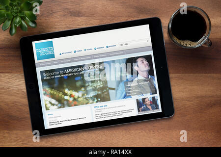 The website of American Express is seen on an iPad tablet, on a wooden table along with an espresso coffee and a house plant (Editorial use only). Stock Photo