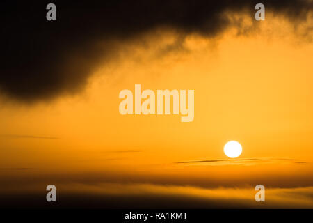 The sun shines in orange as a fireball between two cloud layers Stock Photo