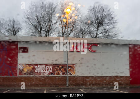 Theside of a KFC outlet seen through a blurry rain spattered car window with the focus on KFC, with a dreary dull wet winter background Stock Photo