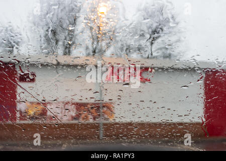 A blurred side of a KFC outlet seen through a rain spattered car window with the focus on the rain drops, with a dreary dull wet winter background Stock Photo