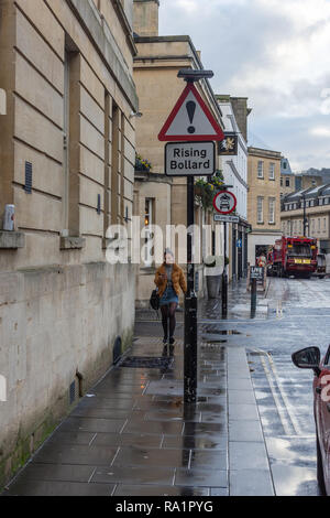 Pedestrian walking towards a triangular caution sign warning of a rising bollard in the road on Lower Borough Walls in the city of Bath Stock Photo