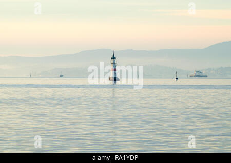 Small white lighthouse isolated on pink sky background at sunset, in entrance to Oslo harbour. Winter time and calm sea in inner Oslofjord waters. Stock Photo