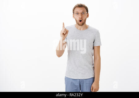 Got excellent idea listen. Stunned excited charming mature guy with bristle gasping opening mouth in surprise while making up great plan raising index finger in eureka gesture over white wall Stock Photo