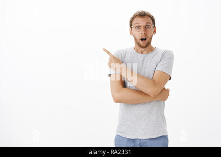 Guy obserbed awesome scene showing friend to look quickly being thrilled and surprised opening mouth from surprise gazing excited at camera and pointing at upper left corner Stock Photo