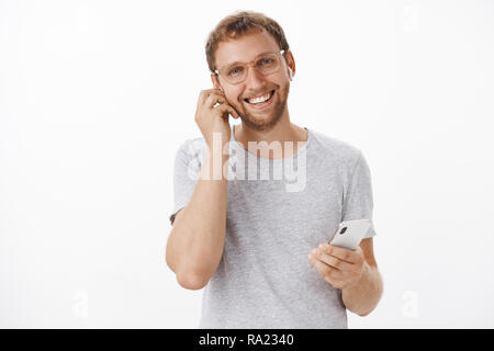 Confident and pleasant european man signing expensive deals on go talking with clients in wireless earphones holding smartphone and smiling friendly and joyful having nice calm conversation Stock Photo