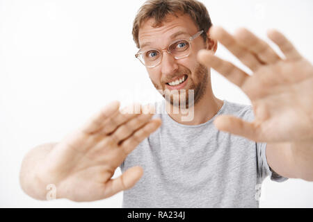 Man feeling shy hates being photographed pulling hands towards camera to cover face from flashlight making confused awkward face raising eyebrows and squinting feeling uncomfortable Stock Photo