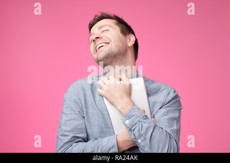 Happy young man holding tablet standing over pink wall Stock Photo