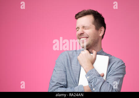 Happy young man holding tablet standing over pink wall Stock Photo