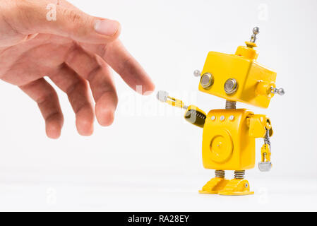 Cute, yellow, handmade robot with a human hand on a white background. Like The Creation of Adam painting of Michelangelo. Stock Photo
