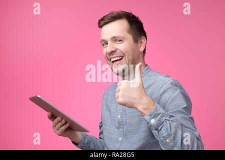 Man holding tablet raising thumbs up and smiling broadly, giving positive feedback Stock Photo