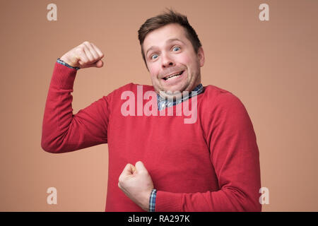 Young funny man in red sweater, shows biceps isolated over white background. Stock Photo