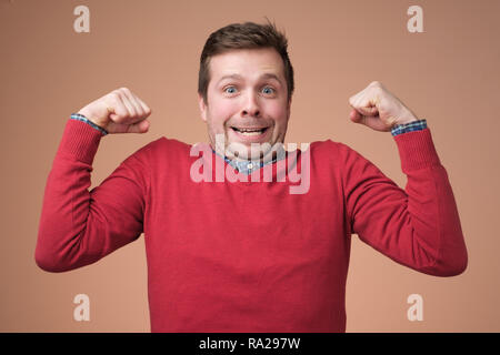 Young funny man in red sweater, shows biceps isolated over white background. Stock Photo