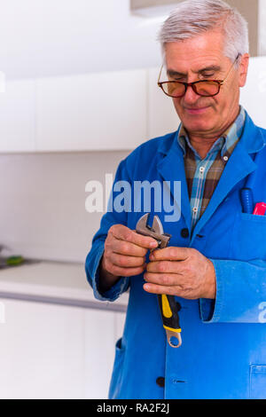 Old age repairman looking happy while holding tool and working Stock Photo