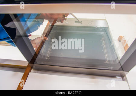 Old handyman is fixing the oven in the kitchen Stock Photo