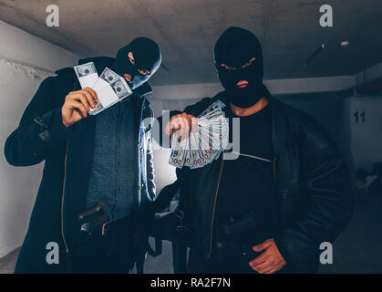 Masked burglars are standing in a dark hallway, holding guns and a bag full of money Stock Photo