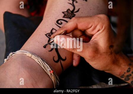 An artist hand freestyle drawing a henna tattoo design up a ladies leg Stock Photo