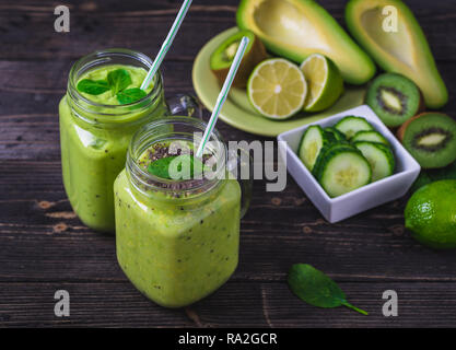 Green smoothie on dark background with avocado, spinach, lemon and kiwi on the right side. Stock Photo