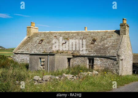 An old abandoned stone croft house with a stone wall on the Mainland island of the Orkney Islands in northern Scotland Stock Photo