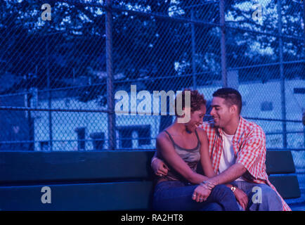 Young Urban ethnic couple flirting on a park bench at dusk or early evening Stock Photo