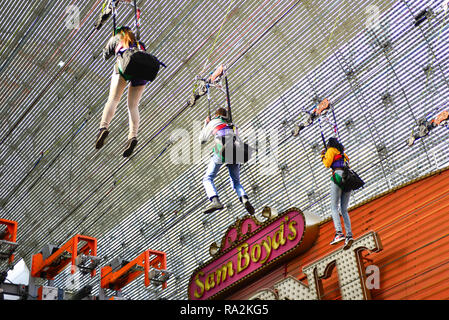 Three people hang from the barrel vault canopy ceiling at the Fremont Street Experience while flying the SlotZilla Zip Line attraction in Las Vegas NV Stock Photo