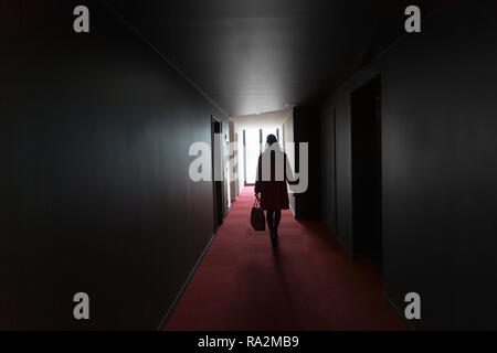 Girl walking through dark hallway in silhouette with bright light beaming through window. Stock Photo