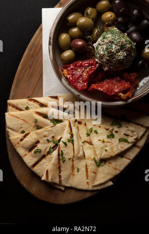Pita bread served with sun dried tomatoes, olives & tzatziki dip on a wood serving board. Stock Photo