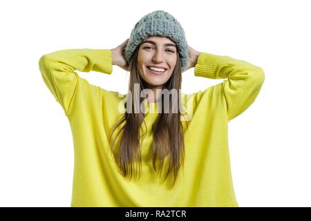 Young cheerful beautiful woman in yellow sweater and gray big loop knitted beanie hat looking at the camera on white isolated background. Stock Photo