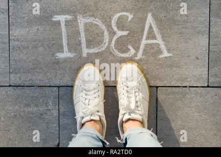 View from above, female feet with text idea written on grey sidewalk. Stock Photo