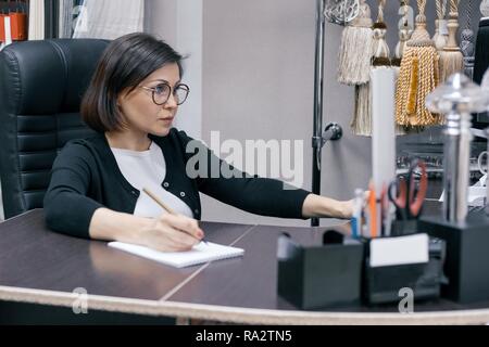 Mature businesswoman in the workplace, woman in the office using computer, background showroom interior fabrics and accessories. Stock Photo