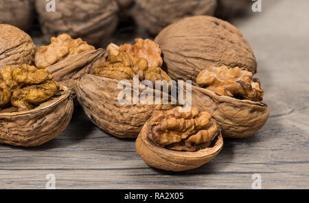 Group of partly peeled nuts with half shells closeup. Cracking of walnuts. Halves of cracked nutshells with nut meat on a wooden background. Walnuts. Stock Photo