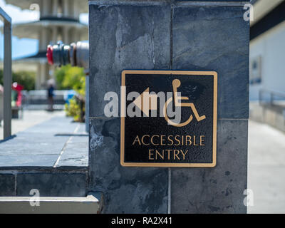 Gold and black accessible entry sign posting with wheelchair handicap logo with arrow pointing to left Stock Photo