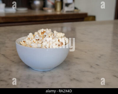 Small mound of fresh popcorn in porcelain bowl sitting on a marble counter