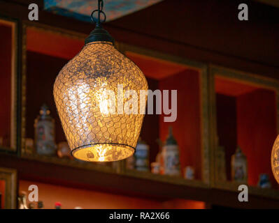 Glass and wire lamp cover on a hanging light bulb in dark bar Stock Photo