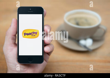 A man looks at his iPhone which displays the Peachy logo (Editorial use only). Stock Photo