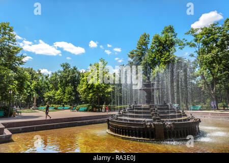 Chisinau, Moldavia - July 4th 2018 - Locals and tourists walking around a beautiful water fountain in a open air park with trees and blue sky Stock Photo