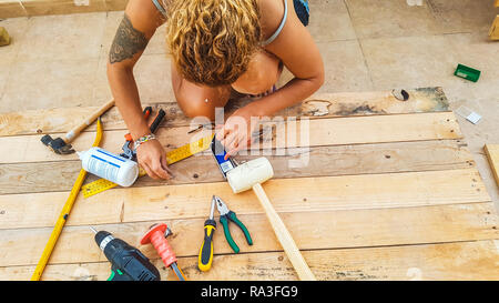 Middle age caucasian woman repairing and building furnitures using recycled wood from cargo pallets outdoor - hardware and all necessary for work leis Stock Photo