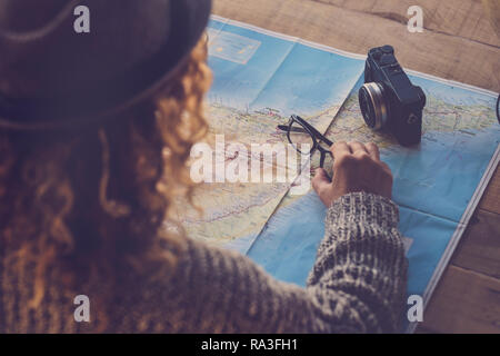Curly lady viewed from rear planning next trip vacation wanderlust on a paper map and old camera on the table - planning holday and travel concept for Stock Photo