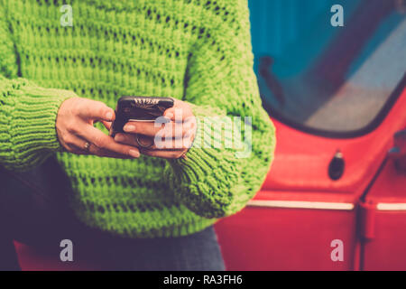 Close-up female hands using and messaging with modern technology smart phone - green jackets and red old vintage car in background - coloured lifestyl Stock Photo