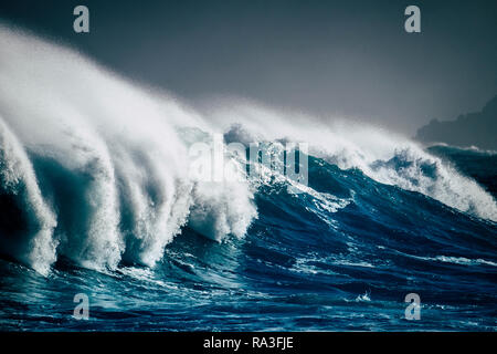 Big wave crash in the middle of the ocean with cliffs and coast in background - white splash for big swell and tide perfect for surfers - dangerous bl Stock Photo