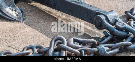 Heavy iron metal ship anchor with chain on gray asphalt. Close-up. Stock Photo