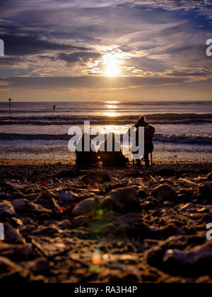 Three people sitting on West Wittering beach wrapped up in winter clothes. Chichester, West Sussex, UK Stock Photo