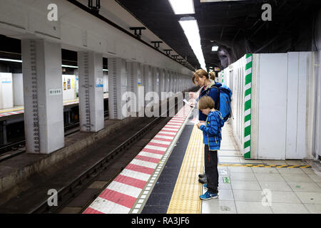 Western mother and son travelers waiting in the underground for a passing train, Tokyo Stock Photo