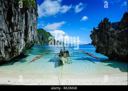 Outrigger boat on a little white beach and crystal clear water in the Bacuit archipelago, Palawan, Philippines Stock Photo