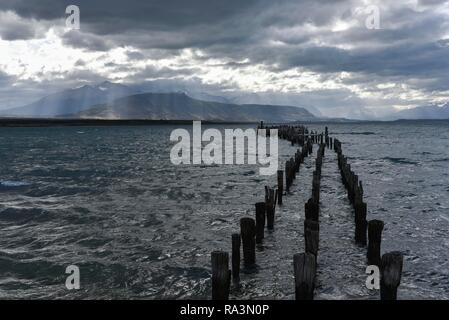 Sunbeams break through dark clouds, decayed jetty, behind Isla Diego Portales, Puerto Natales, province Última Esperanza, Chile Stock Photo