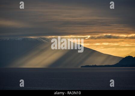 Sun rays shine through dark cloudy sky in front of Osorno Volcano at Llanquihue Lake, sunrise, Puerto Varas, Carretera austral Stock Photo