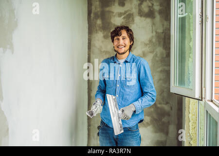 master is applying white putty on a wall and smearing by putty knife in a room of renovating house in daytime Stock Photo